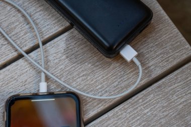Güç bankasından şarj olan telefonun yakın çekimi. Şarj etmek için bir cep telefonunu beyaz kabloyla aküye bağlamak. Yüksek kalite fotoğraf