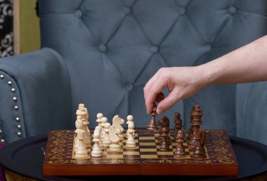 Beyaz tenli bir adamın eli satranç tahtasının üzerinde siyah bir piyon taşını tutuyor. Bir oyun sırasında bir satranç oyuncusunun elinin yakın çekimi.