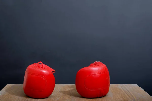 A beautiful set of two red lady\'s leather boxing gloves are on the light wooden table near a dark grey wall as a background, ready for competition for weekend activity. Studio photo.