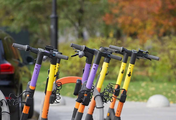 いくつかの明るい色の電動スクーターは秋の公園の駐車場に立っています 休暇中の人々のための生態系の輸送 午後の秋の公園 — ストック写真