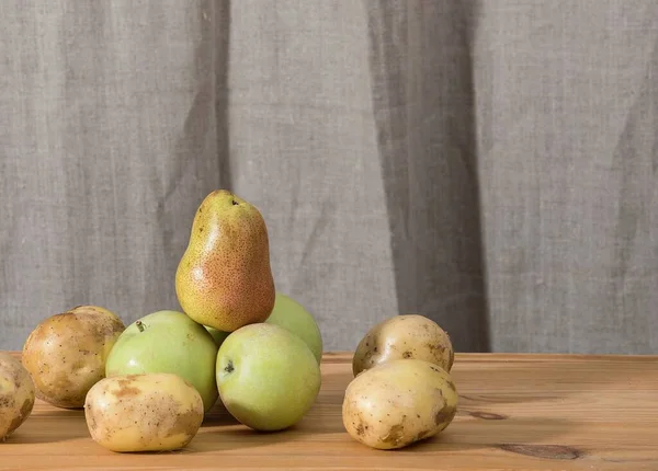 Ripe juicy autumn pears and green apples are stacked in a large pyramid on a structure wooden rustic table at the farm House in a photo studio with a natural linen background. Plenty of space for text
