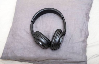 Müzik dinlemek için şık siyah kulaklıklar yatak odasındaki küçük gri bir yastığın üzerinde yatıyor. Stüdyo fotoğrafçılık.