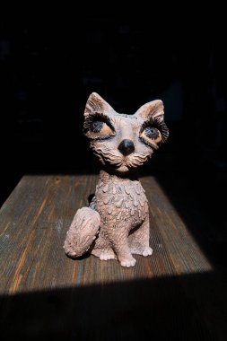Tahta bir kedi heykelciği sabah güneşinin parlak bir noktasında duruyor. Heykel, evin rahatlığını simgeliyor..
