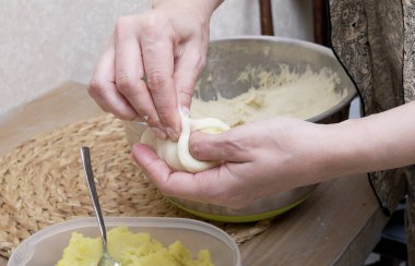 Kadınların elleri, sıcacık çiftlik evinin ahşap masasındaki ev mutfağında sıcak hamura sarılan patates püresini dikkatlice tutuyor. El yapımı turta hazırlama süreci.