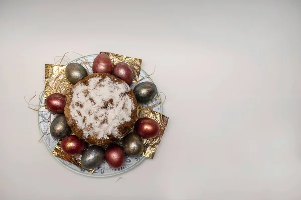 On the religious holiday of Easter, a cooked Easter cake stands on a plate with chicken eggs painted in different colors, top view. Studio photography on a white background.