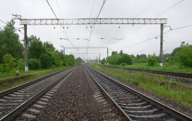 Islak demiryolu rayları ve yağmurlu bir yaz günü yağmurlu havada uyuyanlar ve gökyüzünde gri alçak bulutlar. Bulutlu havada demiryolu kavşağı.
