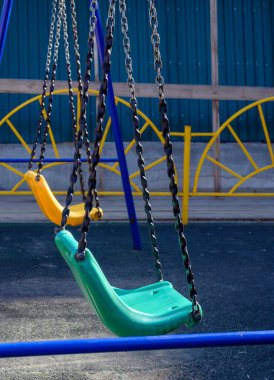 Bahçede boş bir plastik salıncak, mavi metal bir çite zincirlenmiş yeşil ve sarı. Sabah parlak ışık bir salıncakta düşer.