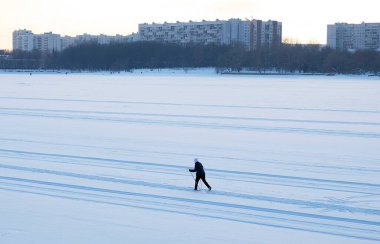 Şehirdeki donmuş bir nehrin yatağında kayak yapan bir kayakçının silüeti. Bir kış günü gün batımında evlerin arasında yürü..