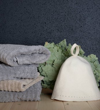 Fees for visiting the Russian bath such as a bio green bath broom surrounded by a washcloth and large bath towels and special sauna hat are situated on the wooden surface. Black backgrounded photo.
