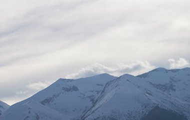 Gün ışığında karla kaplı dağ zirvesi parlak gökyüzüne karşı duruyor, aşağıdaki dağ yamacına gölge düşürüyor. Bu çarpıcı fotoğrafta nefes kesici doğal güzellik var..