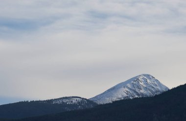 Gün ışığında, parlak gökyüzü ve gölgeli yamaçla karlı dağ zirvesi. Dağın bir tarafı gölgeli, güneşli yamaçlarla çarpıcı bir kontrast oluşturuyor..