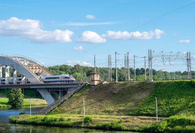 Moskova, Rusya. 25-06-2020. Modern markalı yüksek hızlı yolcu treni Moskova bölgesinde nehrin üzerindeki köprüden geçiyor. Yaz güneşli hava ve bulutlu gökyüzü