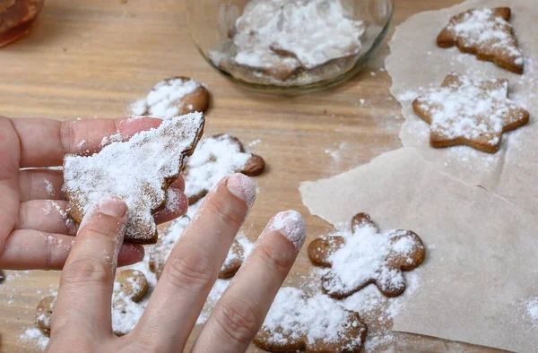 Women\'s hands preparing home baked goods, close-up photo. Hands holding freshly baked cookies over the kitchen table where the process of preparing treats for a holiday is underway. Top view.