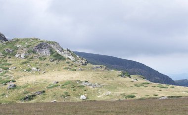 Güneşli bir yaz gününde güneş ışığıyla aydınlanan dağ zirvesi. Dağ yeşil çimlerle kaplıdır. Panoramik fotoğraf.