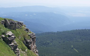 Dağ zirvesinin çıkıntısı diğer sıradağların arka planında parlak sabah güneşinin ışınlarında yeşil çimlerle kaplıydı. Dağ manzarasının görkemli manzarası.