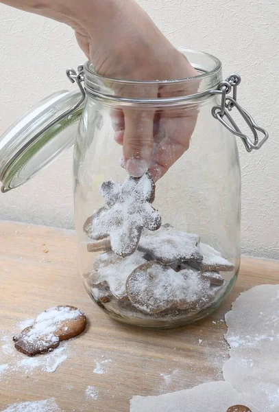 A womans hand takes out a festive cookie for the winter holidays from a glass jar. Close-up of a hand and freshly made delicious cookies that are taken out of a transparent glass jar on a festive day