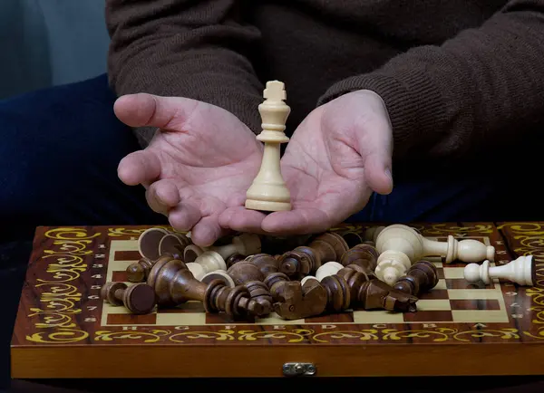 A chess piece in men's over the game board after the end of a game. Cozy living room atmosphere.