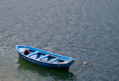 Mavi renkli ahşap bir tekne rüzgarlı güneşli havada suda yüzer. Kürekleri olmayan eski ahşap bir teknenin üst görüntüsü..