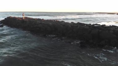 drone video of a man fishing on a jetty at sunset