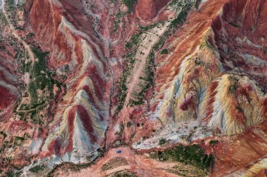 Rengarenk toprak renkleri manzarayı şekillendirir, engebeli dağ oluşumlarını gösterir. Yalnız bir araç, temiz gökyüzünün altında, doğal güzelliklerle çevrili, toprak yolda dinleniyor..
