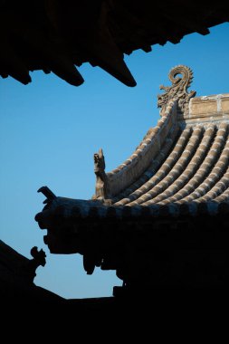 Bir tapınağın tepesinde detaylı çatı süslemeleri bulunan antik Çin mimarisinin çarpıcı görüntüsü. Zarif kıvrımlar ve karmaşık tasarımlar parlak mavi gökyüzü ile çok güzel tezat oluşturuyor..