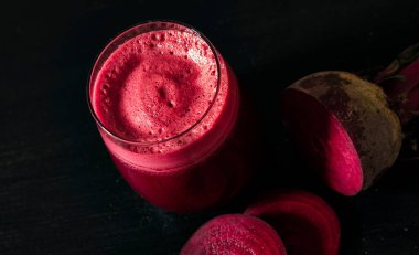 Koyu arkaplanda pancar dilimleri olan bir bardakta taze pancar suyu.