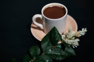 Koyu arkaplanda Türk kahvesi, beyaz porselen bardak, ahşap fincan, beyaz çiçek dallı kompozisyon, rahatlatıcı içecek.