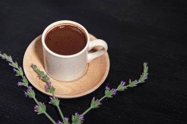 Beyaz porselen fincanda koyu arkaplanda Türk kahvesi, ahşap tabak, geleneksel tazeleyici içecek, lavanta çiçeği.