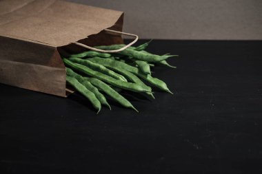 Siyah ahşap arka planda organik kağıt torba içinde çiğ taze fasulye.