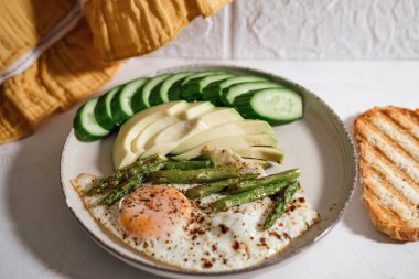 Sabah kahvaltısı, günlük hızlı sağlıklı pişirme, kuşkonmaz, yumurta, salatalık, kızarmış ekmek, beyaz mutfak arka planında avokado.