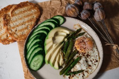 Sabah kahvaltısı, günlük hızlı sağlıklı pişirme, kuşkonmaz, yumurta, salatalık, kızarmış ekmek, beyaz mutfak arka planında avokado.