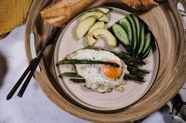 Sabah kahvaltısı sahanda yumurta, haşlanmış kuşkonmaz sarısı, yeşil salatalık ve avokado dilimleri ahşap tepside Fransız ekmeği, düşme, sonbahar masa dekorasyonu ile servis edilir.