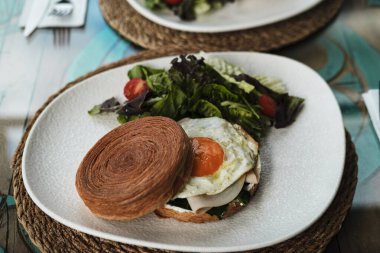 new york roll sandwich with croissant dough, fried egg, cold meat cut,  styled with fresh greens served ready to eat in cafe or restaurant clipart