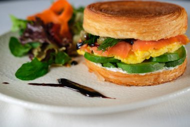 New York usulü sandviç, kruvasan hamurlu, füme somon, avokado, çırpılmış yumurta veya taze yeşillikli omlet.