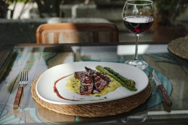  Patates püresi, soğan ve ızgara kuşkonmazla servis edilen fileto restoranın arka planında yenmeye hazır kırmızı şarapla birlikte.