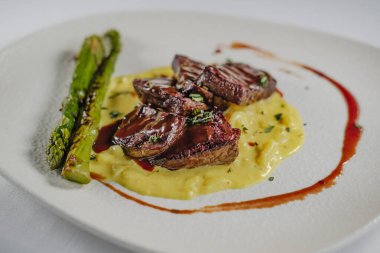 Kırmızı şarap soslu fileto. Patates püresi, soğan, ızgara kuşkonmaz, beyaz tabak ve arka plan.