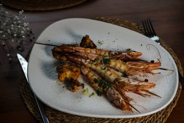 Mantarlı ızgara karides ve tereyağlı sarımsak sosu, üzerinde Akdeniz bitkileri olan çubuklarla servis edilir.