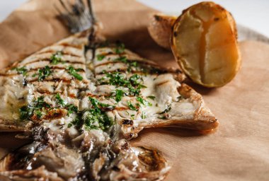 Baharatlı balık fileto sosu, Akdeniz otları, parşömen kağıdı ve tabakta fırında patates ile servis edilir.