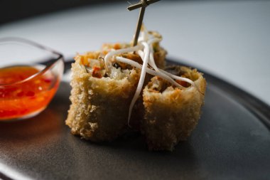 Sebzelerle doldurulmuş kızarmış çıtır börekler, filizlenmiş buğdayla kaplanmış, yoğurt ve tatlı acı biber sosuyla servis edilen siyah kil tabağında.