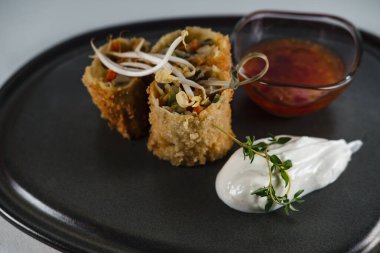 fried crispy spring rolls stuffed with vegetables, topped with sprouted wheat, served on dark clay plate with yoghurt and sweet chili sauce clipart