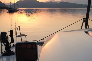 Sabahın sakin manzarası güverteden sakin gün doğumu demirleme yerinde, yükselen güneş, dağlar, deniz ışık yansımaları, alacakaranlık renkleri, yelkenli botlar, dingin liman