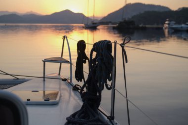 Sabahın sakin manzarası güverteden sakin gün doğumu demirleme yerinde, yükselen güneş, dağlar, deniz ışık yansımaları, alacakaranlık renkleri, yelkenli botlar, dingin liman