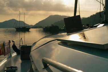 Sabahın sakin manzarası güverteden sakin gün doğumu demirleme yerinde, yükselen güneş, dağlar, deniz ışık yansımaları, alacakaranlık renkleri, yelkenli botlar, dingin liman