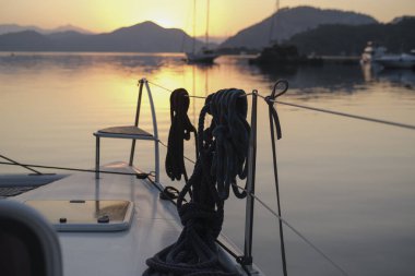 Sabahın sakin manzarası güverteden sakin gün doğumu demirleme yerinde, yükselen güneş, dağlar, deniz ışık yansımaları, alacakaranlık renkleri, yelkenli botlar, dingin liman