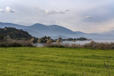 Türkiye 'nin Mugla kentindeki Bafa Gölü' nün panoramik manzarası, düz arazi ve göl, sisli dağlar, yeşil alan, kaya oluşumları arasında tarihi medeniyetlerin kalıntıları.
