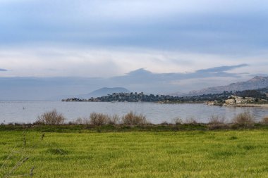 Türkiye 'nin Mugla kentindeki Bafa Gölü' nün panoramik manzarası, düz arazi ve göl, sisli dağlar, yeşil alan, kaya oluşumları arasında tarihi medeniyetlerin kalıntıları.