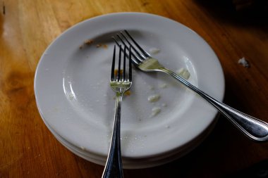 pile of white ceramic plates and stainless forks in a restaurant on wooden table