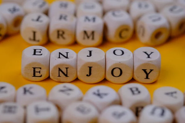 enjoy word concept on wooden cubes blocks on yellow background  