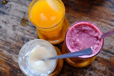 Mango, mulberry, and soursop juice in glasses on a wooden table.