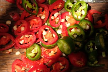 close up of red and green chilies sliced on a brown wooden cutting board